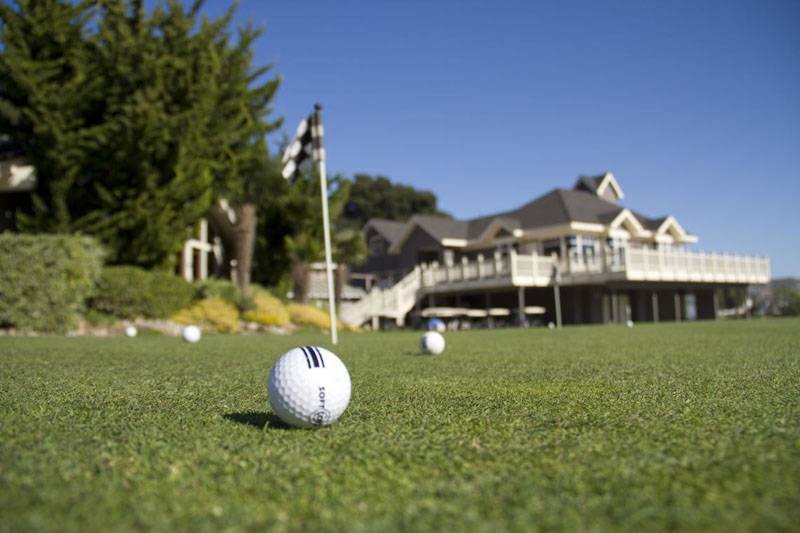 Several golf balls sit on the course in view of the clubhouse at Avila Beachd